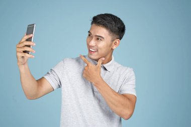 Akıllı telefon ile Asyalı genç yakışıklı çekici adam mavi arka plan üzerinde selfie fotoğraf çekmek