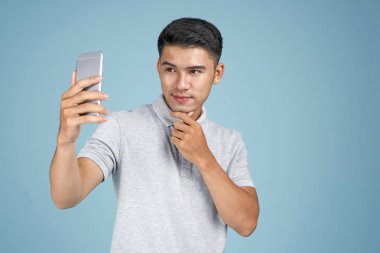 Akıllı telefon ile Asyalı genç yakışıklı çekici adam mavi arka plan üzerinde selfie fotoğraf çekmek