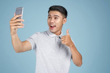 Akıllı telefon ile Asyalı genç yakışıklı çekici adam mavi arka plan üzerinde selfie fotoğraf çekmek