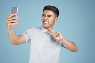 Akıllı telefon ile Asyalı genç yakışıklı çekici adam mavi arka plan üzerinde selfie fotoğraf çekmek
