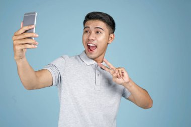 Akıllı telefon ile Asyalı genç yakışıklı çekici adam mavi arka plan üzerinde selfie fotoğraf çekmek