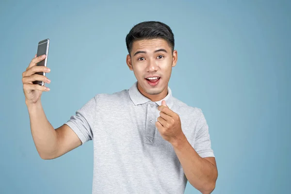 Asiatico giovane bello attraente uomo con smart phone prendere un selfie foto su sfondo blu — Foto Stock