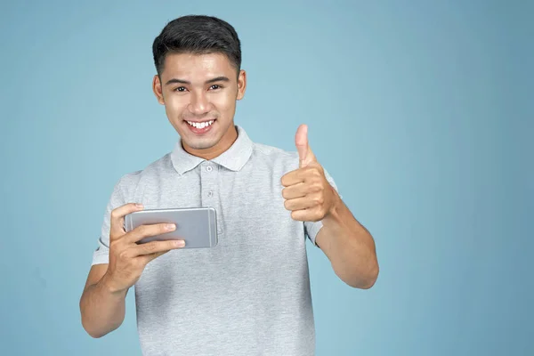 Asiatico giovane bello attraente uomo giocare gioco con smart phone su sfondo blu — Foto Stock