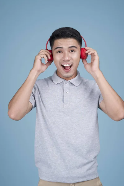 Азиатский молодой привлекательный мужчина слушает музыку с выражением лица на синем фоне — стоковое фото