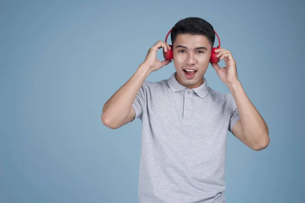 Азиатский молодой привлекательный мужчина слушает музыку с выражением лица на синем фоне — стоковое фото