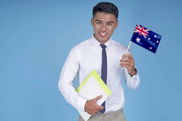 Kitap ve bayrak ile Asyalı genç yakışıklı öğrenci, açık mavi arka plan