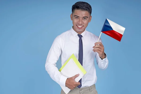 Asian young handsome student with book and flag, on light blue background — Stock Photo, Image