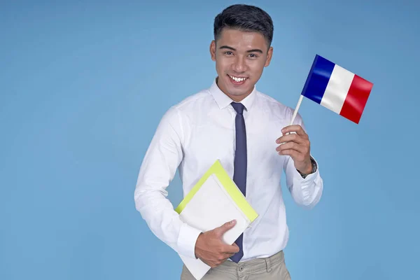 Asiático jovem estudante bonito com livro e bandeira, no fundo azul claro — Fotografia de Stock