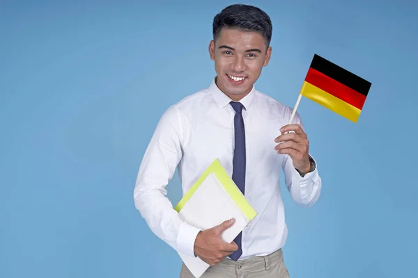 Asian young handsome student with book and flag, on light blue background — Stock Photo, Image