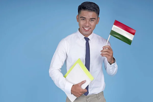 Asian young handsome student with book and flag, on light blue background — Stock Photo, Image