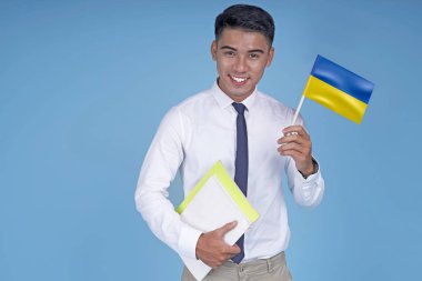Kitap ve bayrak ile Asyalı genç yakışıklı öğrenci, açık mavi arka plan