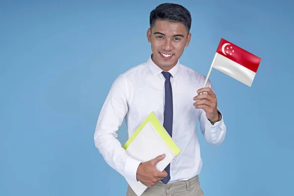 Asian young handsome student with book and flag, on light blue background — Stock Photo, Image