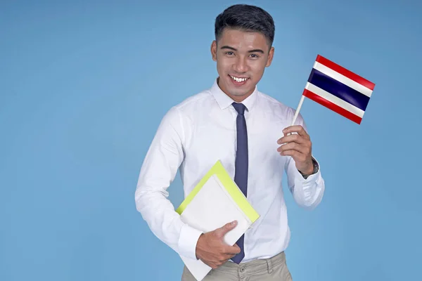 Asian young handsome student with book and flag, on light blue background — Stock Photo, Image