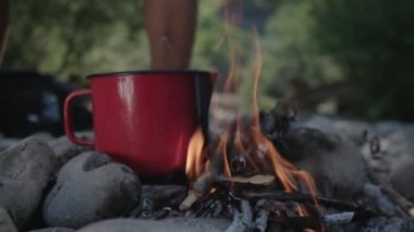 Bir kamp ateşi üzerinde kırmızı bir tencerede kaynar su. 
