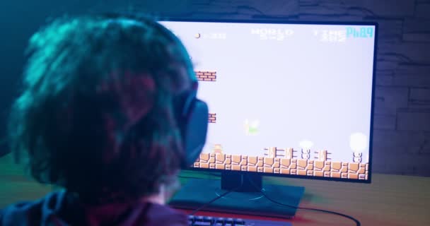 Bakom en gamer med hörlurar som spelar klassiska videospel — Stockvideo