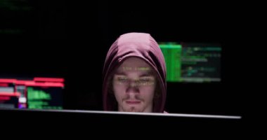 Erkek hacker'kukuleta ile göstermek perde bir karanlık office odada bir bilgisayarda çalışır
