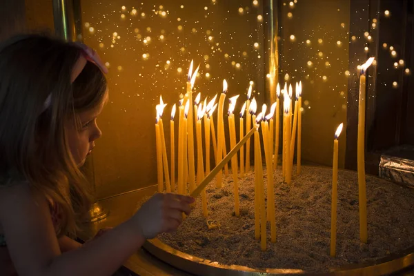 Little girl prays and puts a candle in Orthodox Church