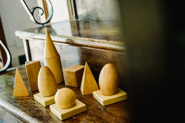 Solid wood shapes to study geometry and volumes, cones, triangles, squares, spheres on a warm wood background.