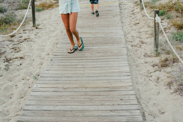 Дети прогуливаются по деревянной тропинке к пляжу летом
