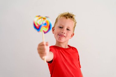 Renkli eğlenceli bir lolipop yemek ve gülerek beyaz zemin üzerine kırmızı gömlek çocukla.
