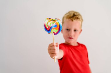 Renkli eğlenceli bir lolipop yemek ve gülerek beyaz zemin üzerine kırmızı gömlek çocukla.