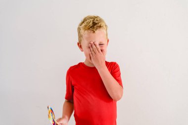 Renkli eğlenceli bir lolipop yemek ve gülerek beyaz zemin üzerine kırmızı gömlek çocukla.