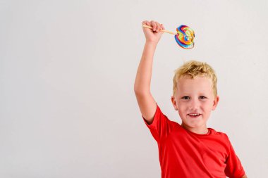 Renkli eğlenceli bir lolipop yemek ve gülerek beyaz zemin üzerine kırmızı gömlek çocukla.