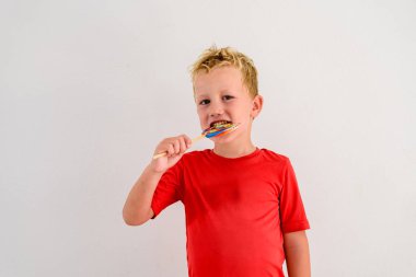 Renkli eğlenceli bir lolipop yemek ve gülerek beyaz zemin üzerine kırmızı gömlek çocukla.