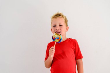Renkli eğlenceli bir lolipop yemek ve gülerek beyaz zemin üzerine kırmızı gömlek çocukla.