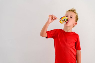 Renkli eğlenceli bir lolipop yemek ve gülerek beyaz zemin üzerine kırmızı gömlek çocukla.