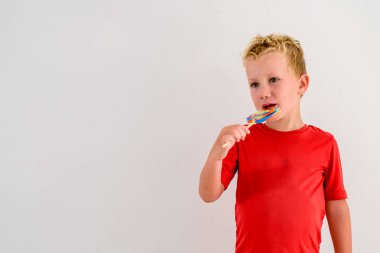 Renkli eğlenceli bir lolipop yemek ve gülerek beyaz zemin üzerine kırmızı gömlek çocukla.