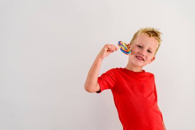 Renkli eğlenceli bir lolipop yemek ve gülerek beyaz zemin üzerine kırmızı gömlek çocukla.