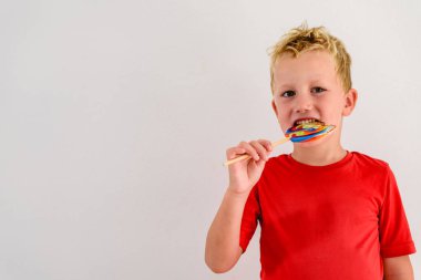 Renkli eğlenceli bir lolipop yemek ve gülerek beyaz zemin üzerine kırmızı gömlek çocukla.