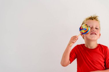 Renkli eğlenceli bir lolipop yemek ve gülerek beyaz zemin üzerine kırmızı gömlek çocukla.