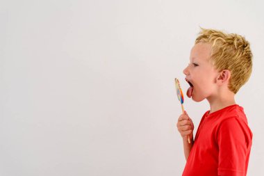 Renkli eğlenceli bir lolipop yemek ve gülerek beyaz zemin üzerine kırmızı gömlek çocukla.