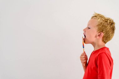 Renkli eğlenceli bir lolipop yemek ve gülerek beyaz zemin üzerine kırmızı gömlek çocukla.