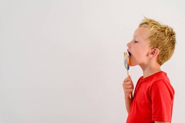 Renkli eğlenceli bir lolipop yemek ve gülerek beyaz zemin üzerine kırmızı gömlek çocukla.