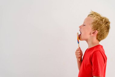 Renkli eğlenceli bir lolipop yemek ve gülerek beyaz zemin üzerine kırmızı gömlek çocukla.