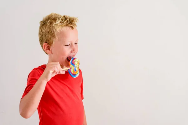 ロリポップ カラフルな楽しみを食べ 笑っている白い背景の赤いシャツの男の子 — ストック写真