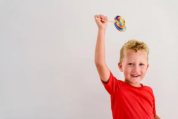 ロリポップ カラフルな楽しみを食べ 笑っている白い背景の赤いシャツの男の子 — ストック写真