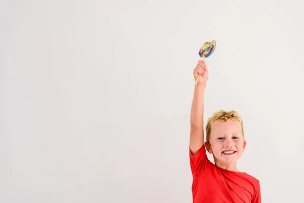 ロリポップ カラフルな楽しみを食べ 笑っている白い背景の赤いシャツの男の子 — ストック写真