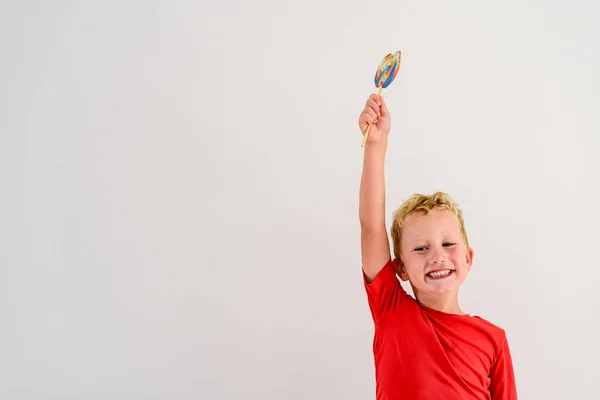 ロリポップ カラフルな楽しみを食べ 笑っている白い背景の赤いシャツの男の子 — ストック写真