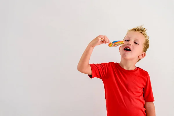 ロリポップ カラフルな楽しみを食べ 笑っている白い背景の赤いシャツの男の子 — ストック写真