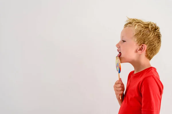 ロリポップ カラフルな楽しみを食べ 笑っている白い背景の赤いシャツの男の子 — ストック写真