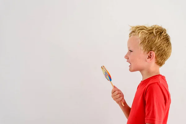 ロリポップ カラフルな楽しみを食べ 笑っている白い背景の赤いシャツの男の子 — ストック写真