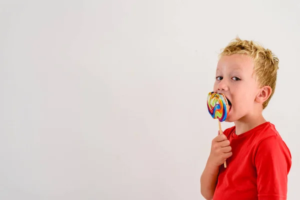 ロリポップ カラフルな楽しみを食べ 笑っている白い背景の赤いシャツの男の子 — ストック写真