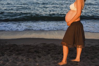 Karın hamile kadının üzerinde plaj, deniz arka planda yürüyen.