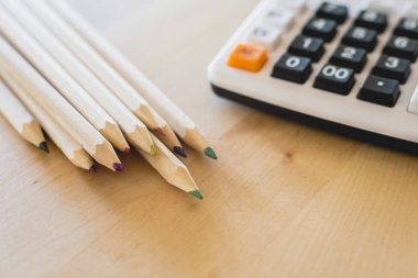 Renkli kalemler ve hesap makinesi bir tablo üzerinde.