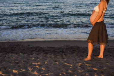 Karın hamile kadının üzerinde plaj, deniz arka planda yürüyen.