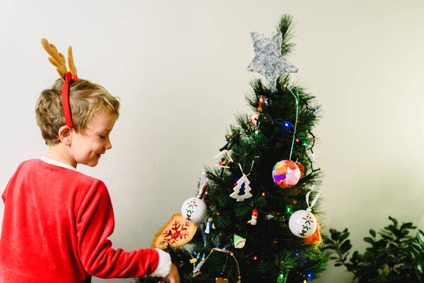 Child in Santa Claus costume, preparing the Christmas tree, back to back and white background with space for text.